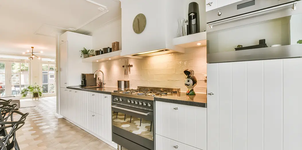 cocina minimalista de color blanco con hornos para cocinar Cocina amplia con todos los muebles situados a lo largo de una pared con muebles blancos y encimera de color negro incluye fuegos de gas y horno en el mismo aparato